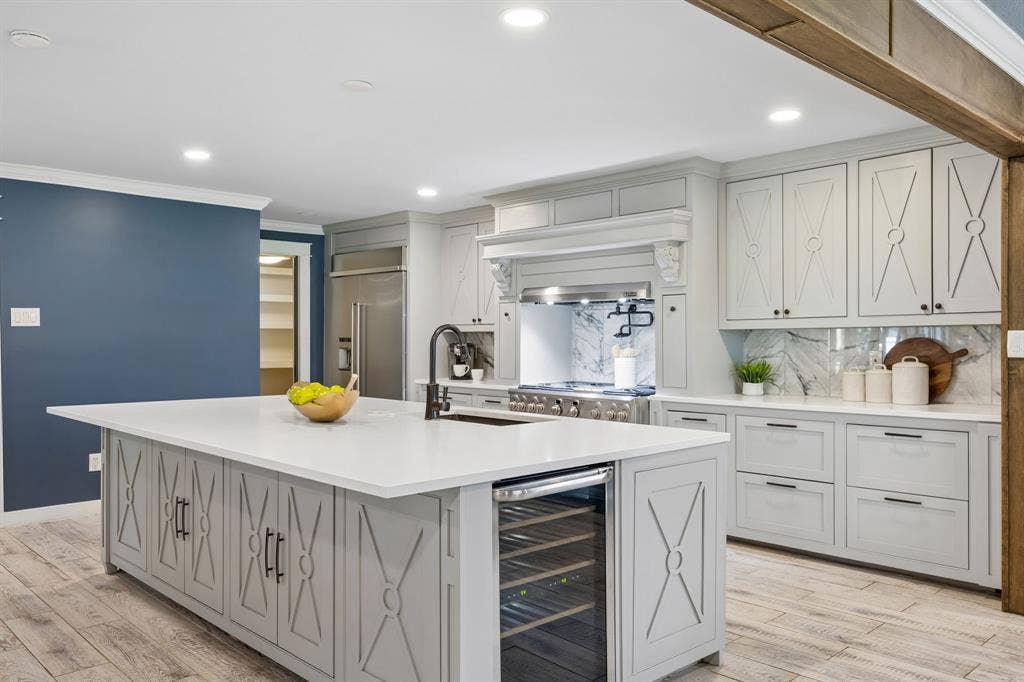 Custom kitchen highlighting the oversized island with built-in wine refrigerator, 6 burner gas range, industrial venthood quartz backsplash and built-in refrigerator.