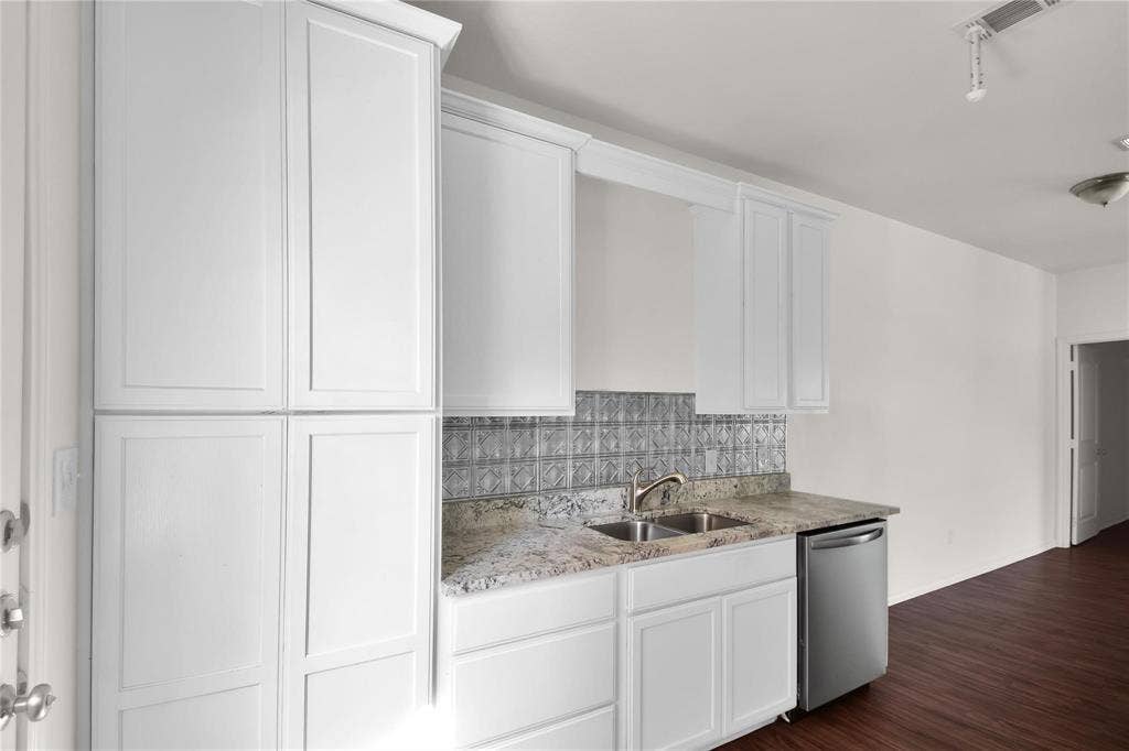 1102 Parkway Trail, Princeton, TX 75407 White shaker cabinetry, stainless steel dishwasher, dual basin sink, patterned tile backsplash, and stone-finish countertop
