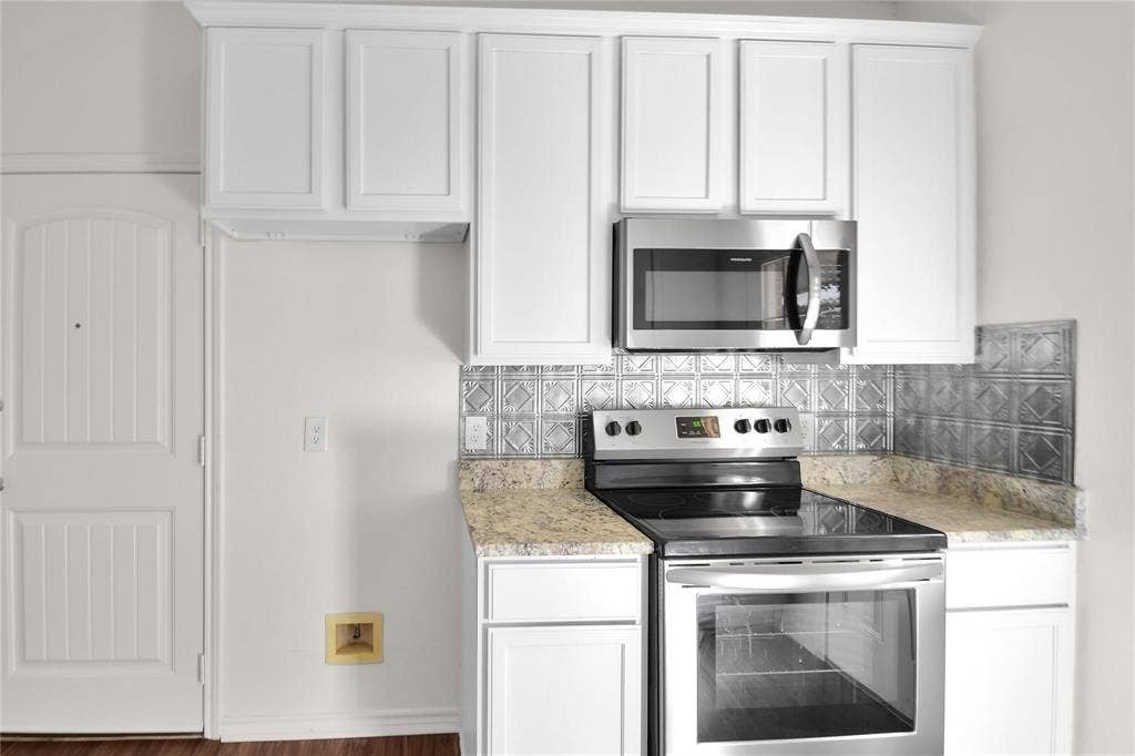 1102 Parkway Trail, Princeton, TX 75407 White paneled cabinetry with stainless steel appliances, granite-style countertops, and a decorative tile backsplash