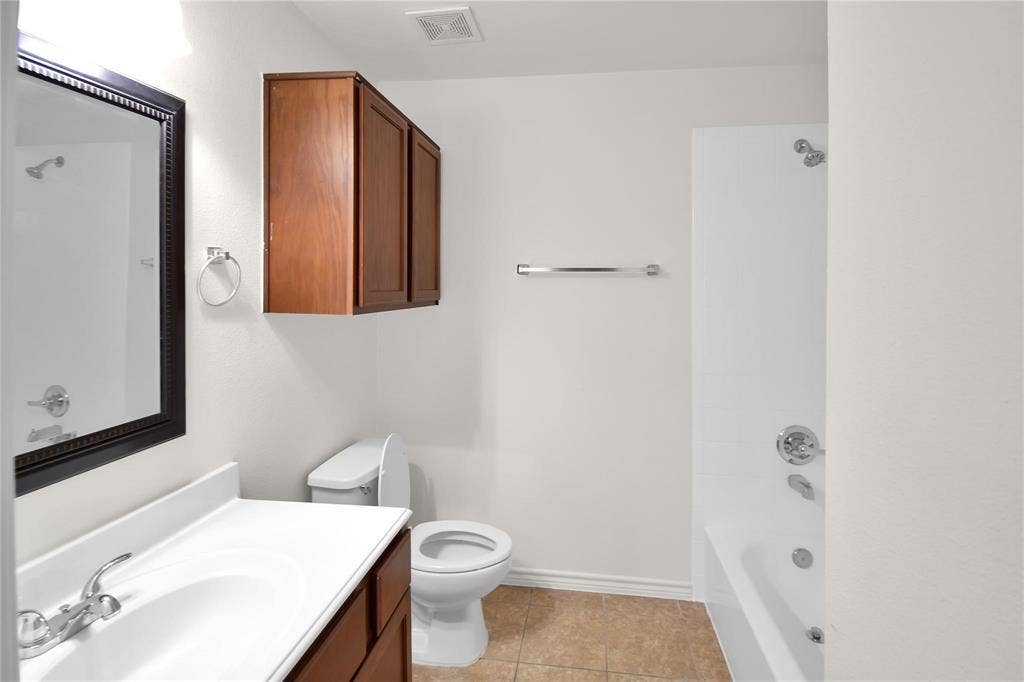 1102 Parkway Trail, Princeton, TX 75407 Bathroom featuring a wood-finish vanity with a white countertop, wall-mounted wood-finish cabinetry, a white toilet, and a white tub with shower