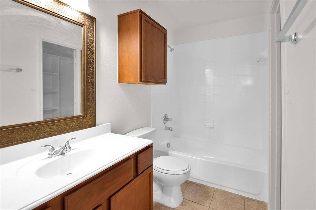 1102 Parkway Trail, Princeton, TX 75407 Bathroom featuring a vanity with a white countertop and wood-finish cabinetry, an ornate framed mirror, a built-in medicine cabinet, a toilet, and a white tub with integrated shower