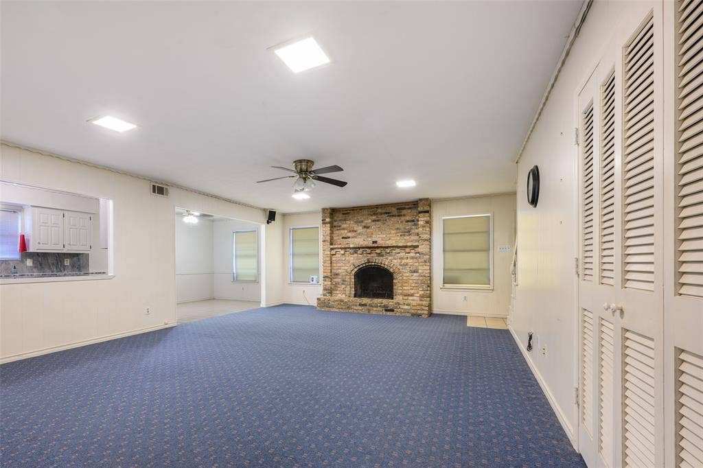 635 Sherrill Boulevard, Duncanville, TX 75116 Spacious room with blue patterned carpeting, a stone-clad fireplace, and white louvered bifold doors