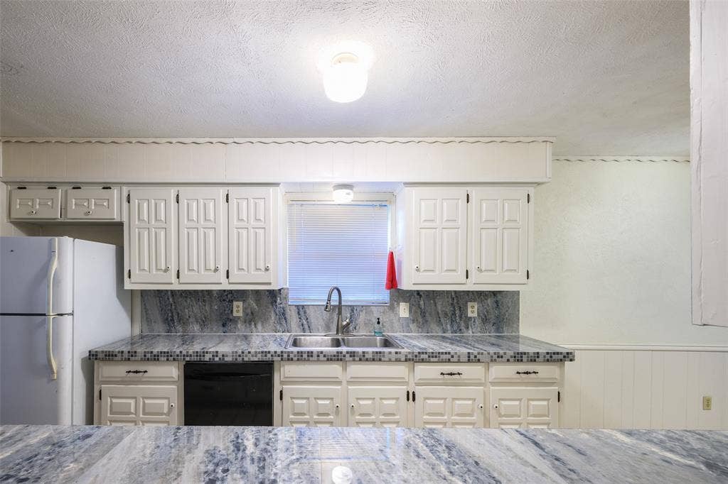 635 Sherrill Boulevard, Duncanville, TX 75116 White cabinetry with dark hardware, dual basin sink with gooseneck faucet, black dishwasher, and stone-look countertops with tile trim