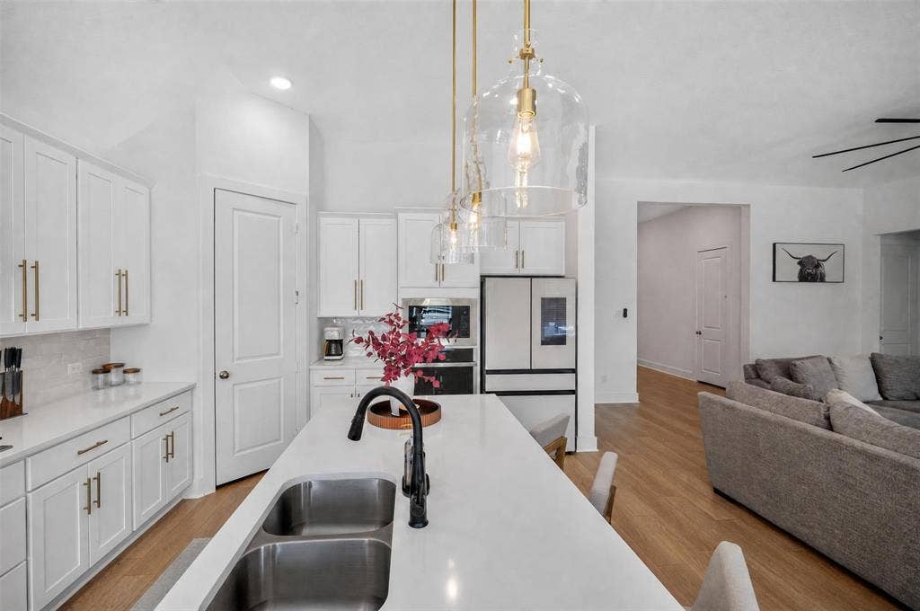 Kitchen featuring a large island with dual-basin sink, white cabinetry with gold-finish hardware, stainless steel appliances, and wood-finish flooring
