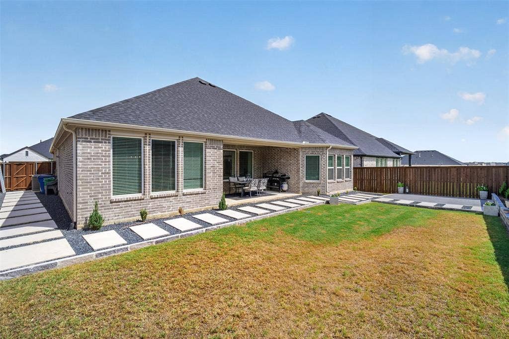 Brick exterior with a covered patio, segmented concrete walkways, a wood privacy fence, and a landscaped yard