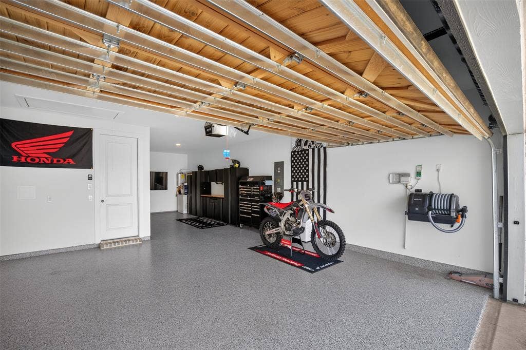 Garage featuring an epoxy coated floor, exposed wood ceiling, white walls, and built-in storage cabinetry