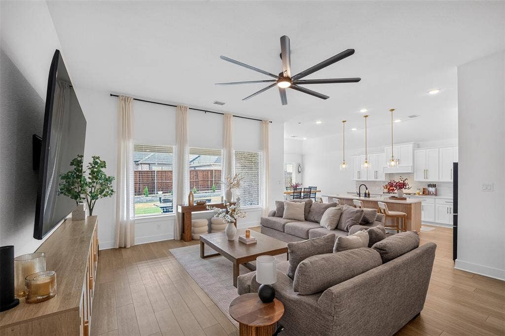 Open-concept living area featuring wood-finish flooring, a contemporary ceiling fan, and large windows