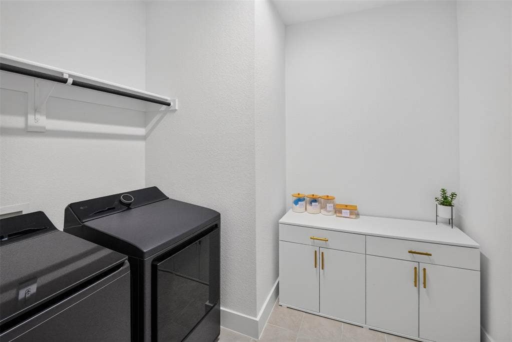 Laundry area featuring a built-in shelf with hanging rod, tile flooring, and white cabinetry with gold-tone hardware