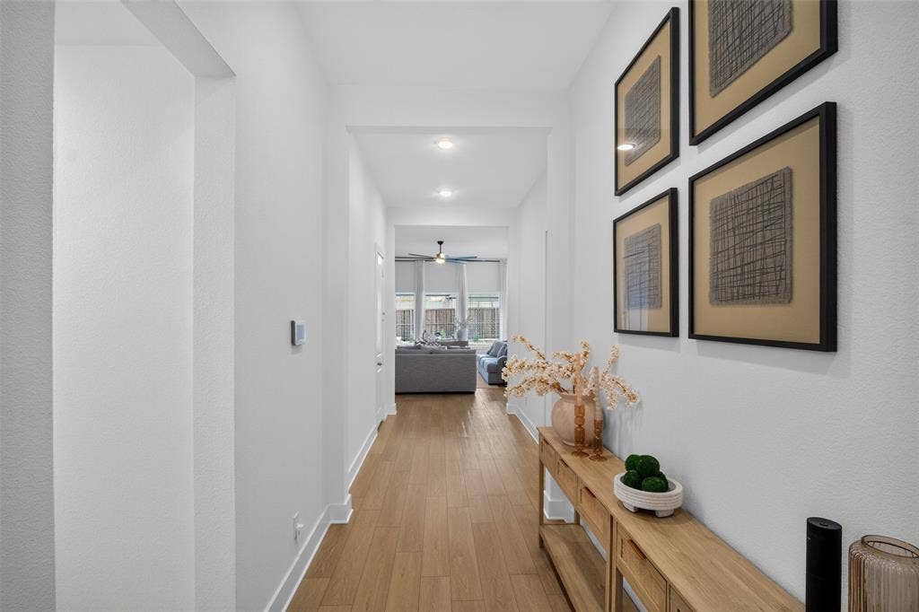 Recessed lighting illuminates wood-finish flooring throughout the hallway, featuring crisp white walls