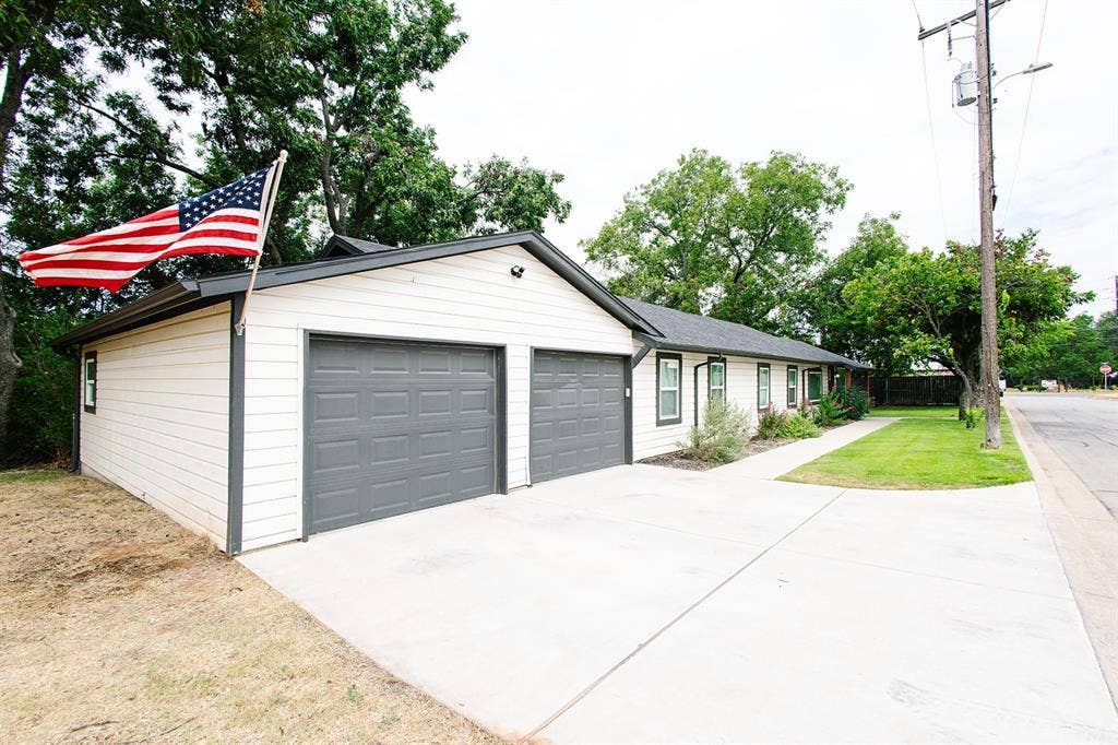 104 S Hawthorne Street, Granbury, TX 76048 White horizontal siding with dark trim, two-car garage with panel doors, concrete driveway, and front walkway