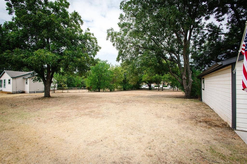 104 S Hawthorne Street, Granbury, TX 76048 Expansive outdoor space featuring mature trees and a detached structure with horizontal siding and dark trim