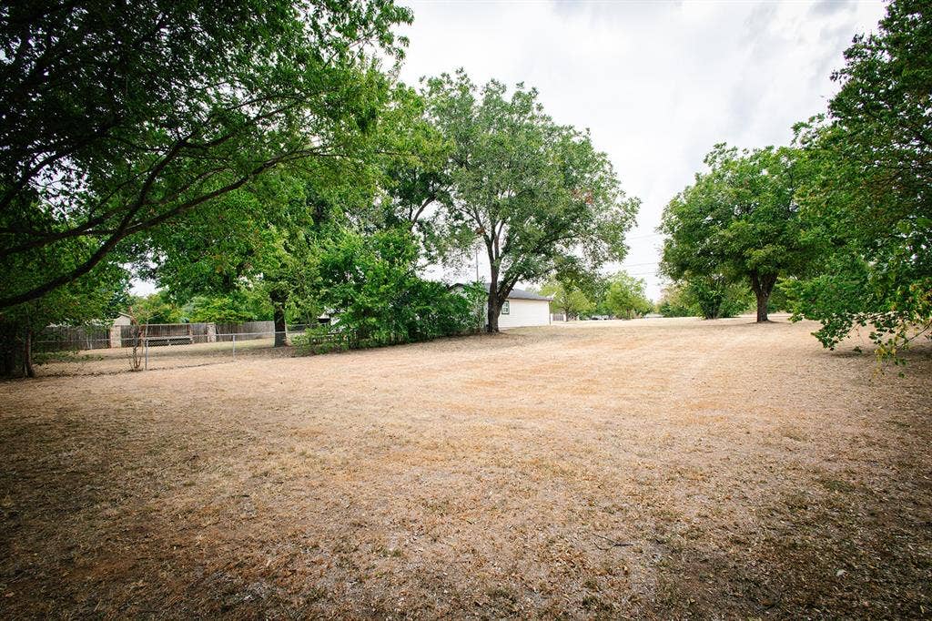 104 S Hawthorne Street, Granbury, TX 76048 Expansive open lot featuring mature trees and a partial perimeter fence