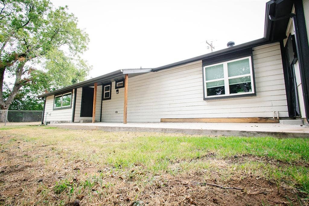 104 S Hawthorne Street, Granbury, TX 76048 Neutral-toned siding with dark trim, featuring multiple windows and a covered entry with wood posts