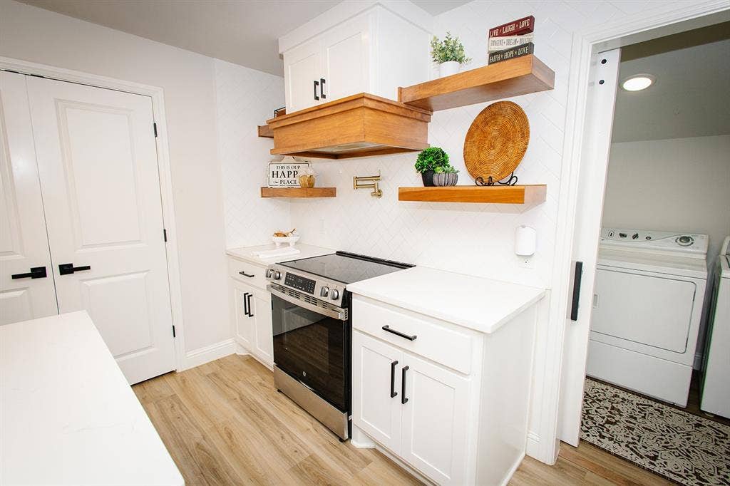 104 S Hawthorne Street, Granbury, TX 76048 White cabinetry with black hardware, wood-finish flooring, stainless steel range, white countertops, and wood floating shelves