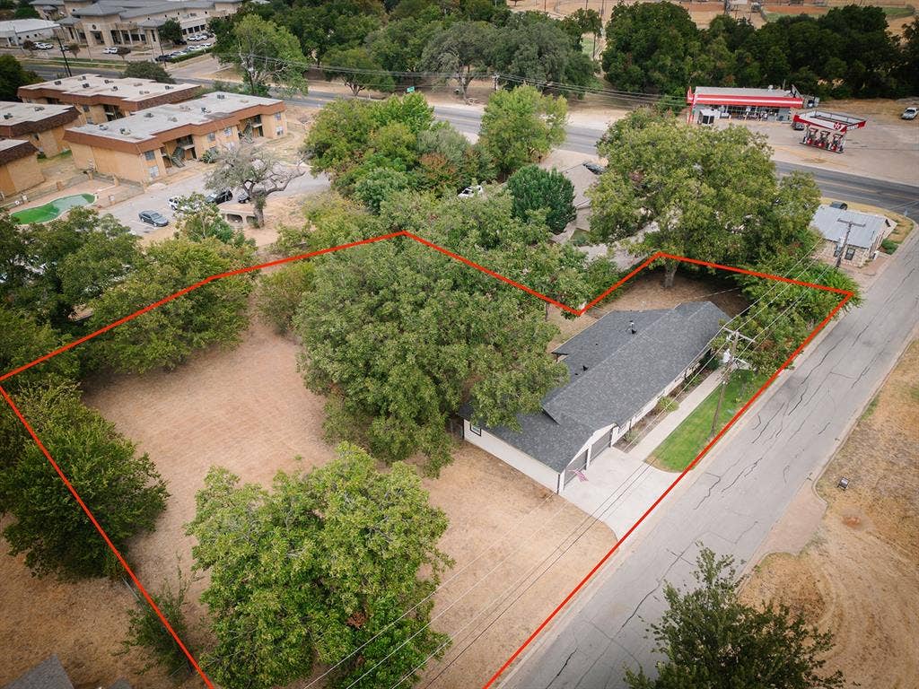 104 S Hawthorne Street, Granbury, TX 76048 Single-story residence with an attached garage, paved driveway, and mature trees on the property