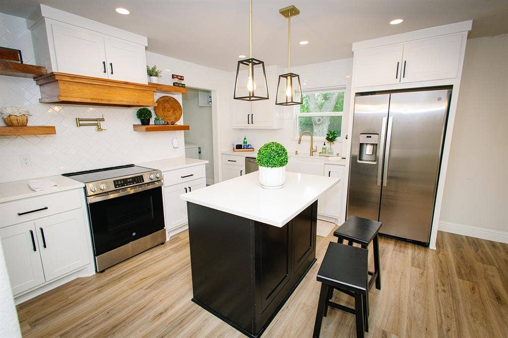 104 S Hawthorne Street, Granbury, TX 76048 White cabinetry, stainless steel appliances, wood-finish flooring, kitchen island with contrasting base, and pendant lighting fixtures