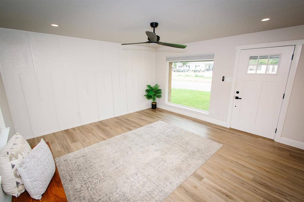 104 S Hawthorne Street, Granbury, TX 76048 Wood-finish flooring, white paneled accent wall, recessed lighting, modern ceiling fan, and white entry door with frosted glass