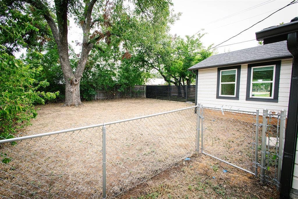 104 S Hawthorne Street, Granbury, TX 76048 Separate fenced area Expansive backyard featuring a mature tree, chain-link fencing, and a dark slat fence