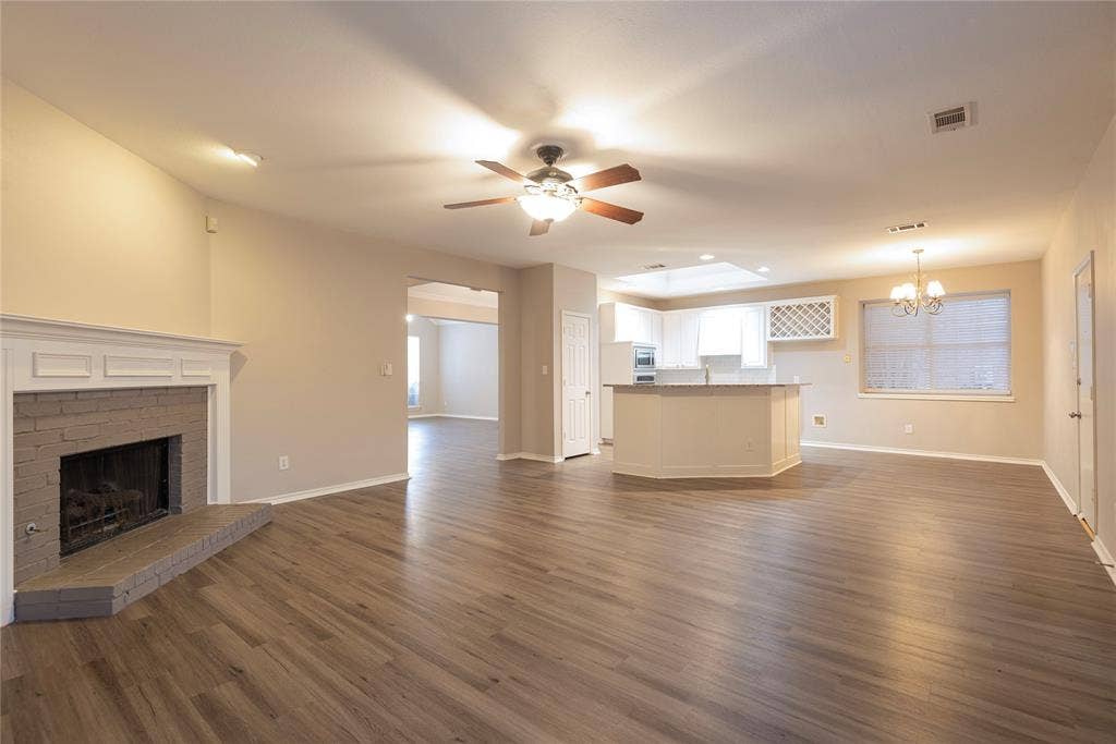 7829 Case Drive, Plano, TX 75025 Unfurnished living room with a fireplace, ceiling fan with notable chandelier, and dark wood-type flooring