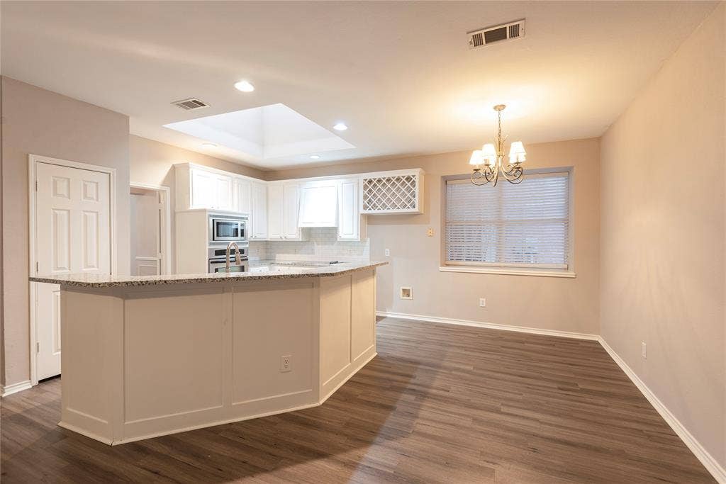 7829 Case Drive, Plano, TX 75025 Kitchen featuring light stone countertops, decorative light fixtures, white cabinetry, and a kitchen island with sink
