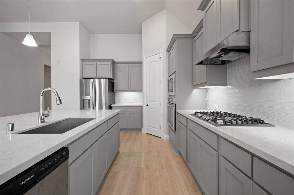 Kitchen featuring light wood-finish flooring, stainless steel appliances, a gas cooktop with an overhead exhaust hood, gray cabinetry, and light-toned countertops