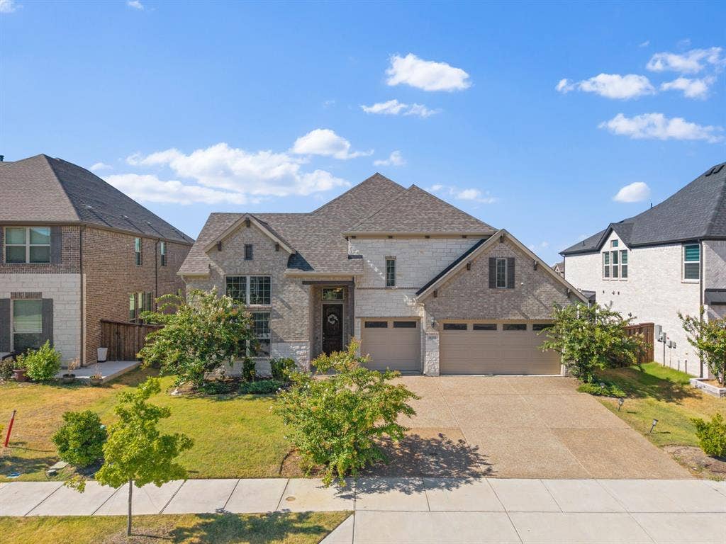 Stone and brick facade with a multi-car garage, mature landscaping, and an aggregate driveway