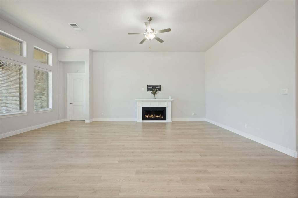 Spacious room featuring wood-finish flooring, multiple windows, a white fireplace, and a ceiling fan