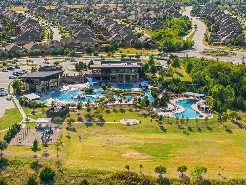 Community recreation area featuring multiple swimming pools, a water slide, shaded lounging areas, and a playground