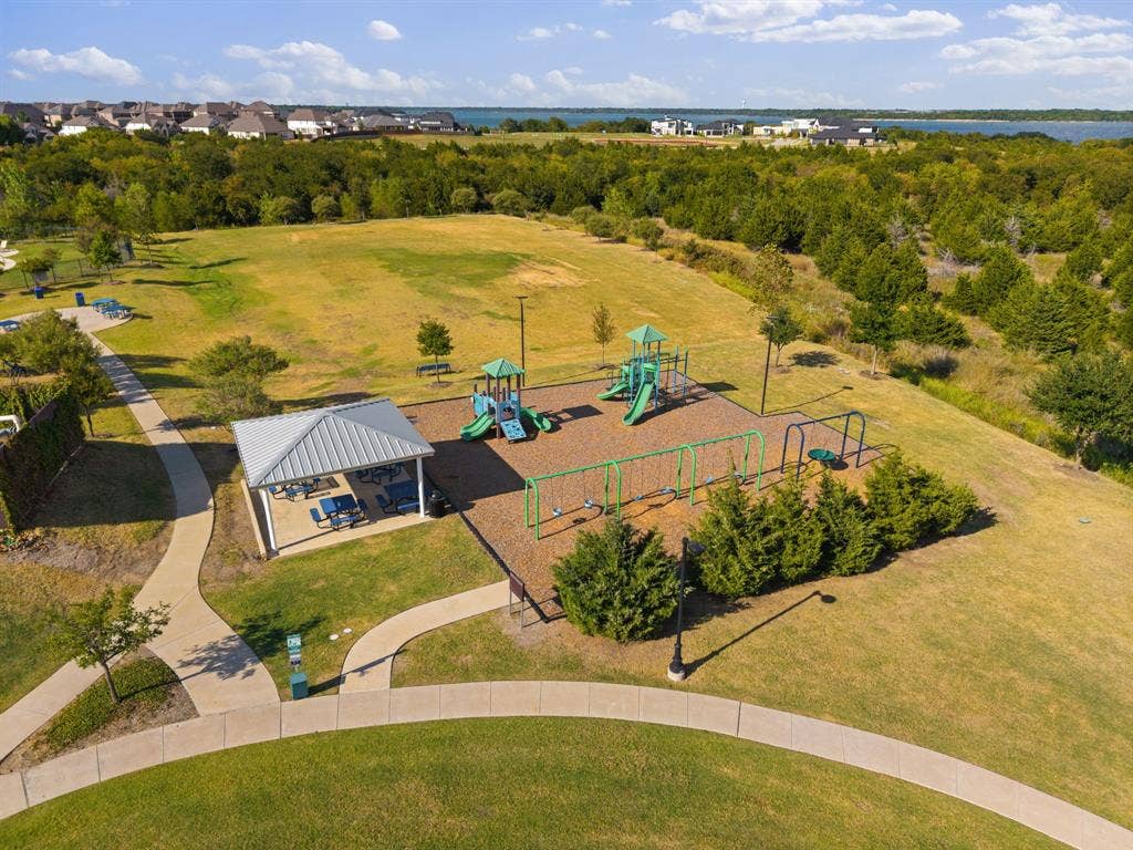 Grassy park area featuring a playground, swing set, covered picnic area, and paved walking paths
