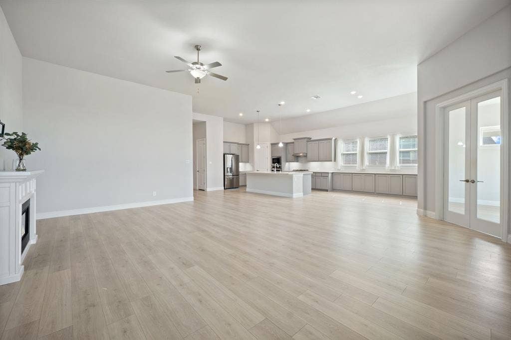 Spacious interior featuring wood-finish flooring, a fireplace with a white mantel, and a ceiling fan with integrated lighting