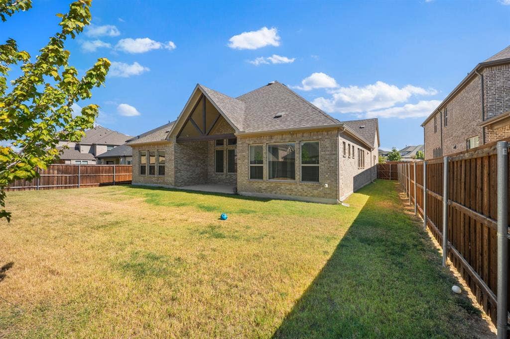 Expansive backyard with a wood privacy fence, covered patio, and brick exterior