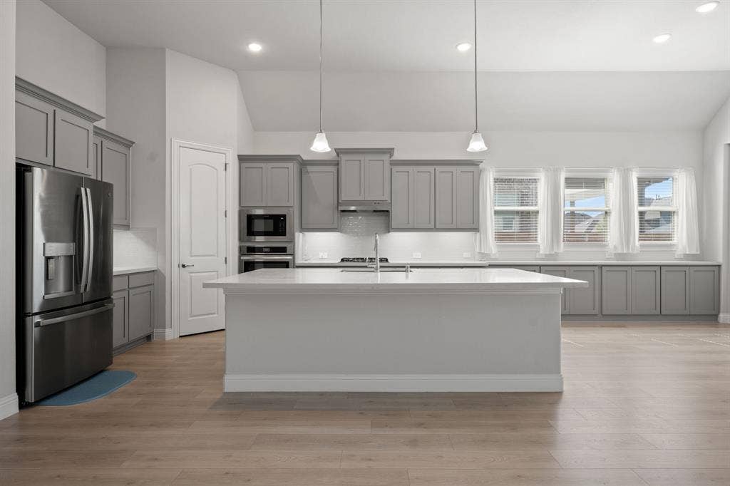 Kitchen featuring light wood-finish flooring, gray cabinetry, a central island with white countertops, stainless steel appliances, and recessed lighting