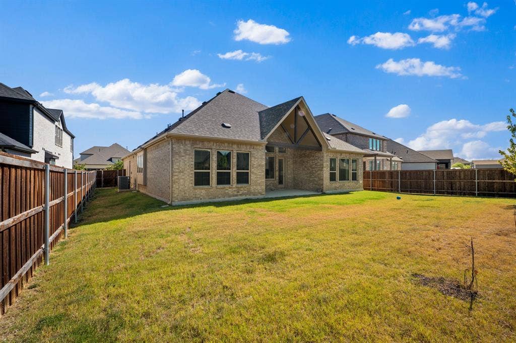 Expansive backyard featuring a covered patio, brick exterior, multiple windows, and a wood privacy fence