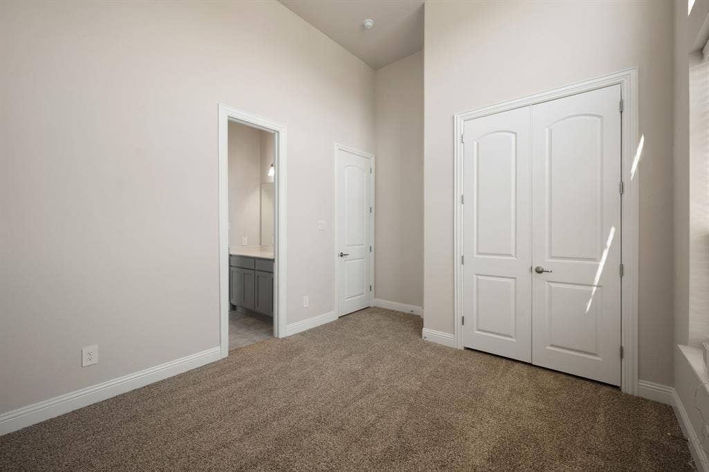 Carpeted flooring, vaulted ceiling, white interior doors, and a bathroom vanity with a light-colored countertop