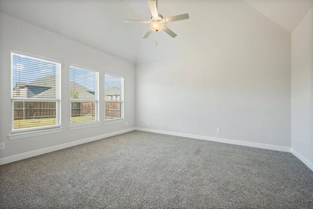 Vaulted ceiling with a ceiling fan, three windows with blinds, light gray walls, and gray carpeting