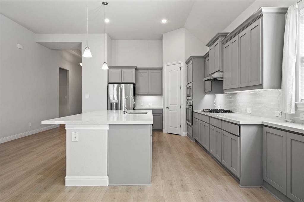 Kitchen featuring light wood-finish flooring, gray shaker-style cabinetry, a white subway tile backsplash, white countertops, and stainless steel appliances