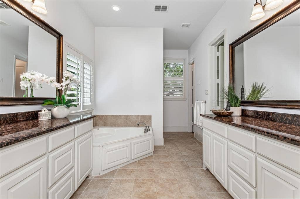 Dual vanity with rich-toned countertops, white cabinetry, undermount sinks, and framed mirrors