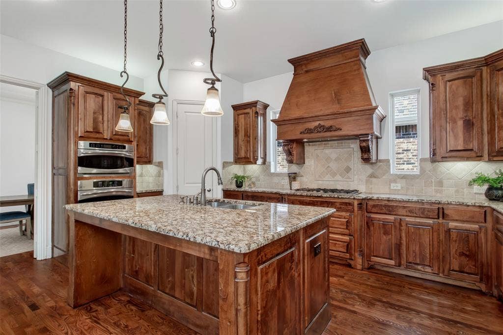 Kitchen featuring wood-finish flooring, wood cabinetry, granite countertops, a built-in oven, and a decorative range hood