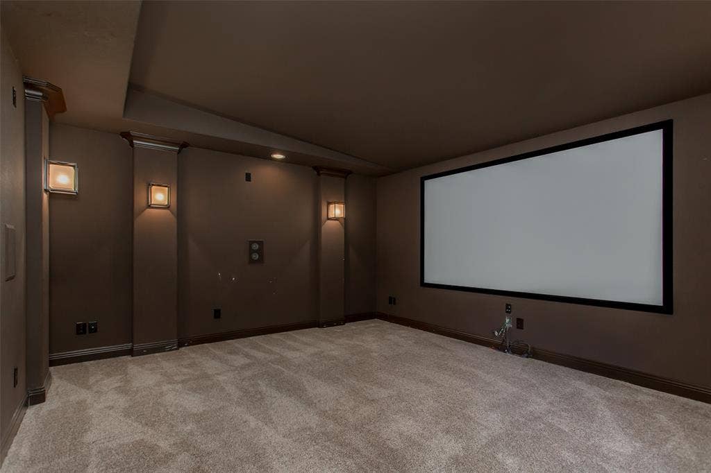 Media room featuring a large projector screen, wall sconces, recessed lighting, and carpeted flooring
