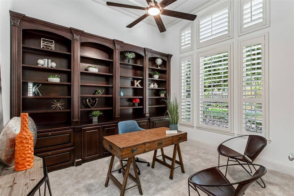 Built-in cabinetry with dark wood finish, multiple window panels with plantation shutters, ceiling fan with integrated lighting, and vaulted ceiling
