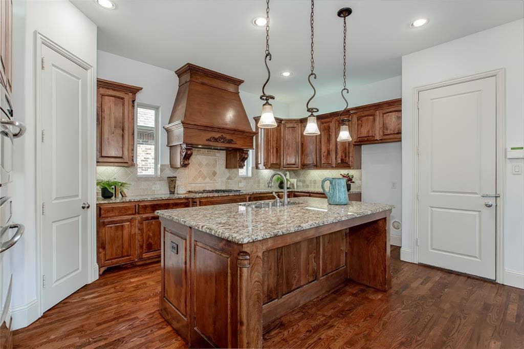 Hardwood flooring, wood-finish cabinetry, granite countertops, decorative range hood, and recessed lighting