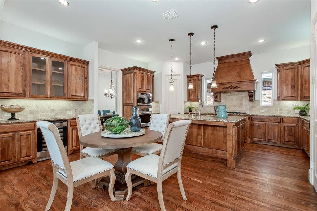 Hardwood flooring, custom wood cabinetry, granite countertops, tile backsplash, and recessed lighting