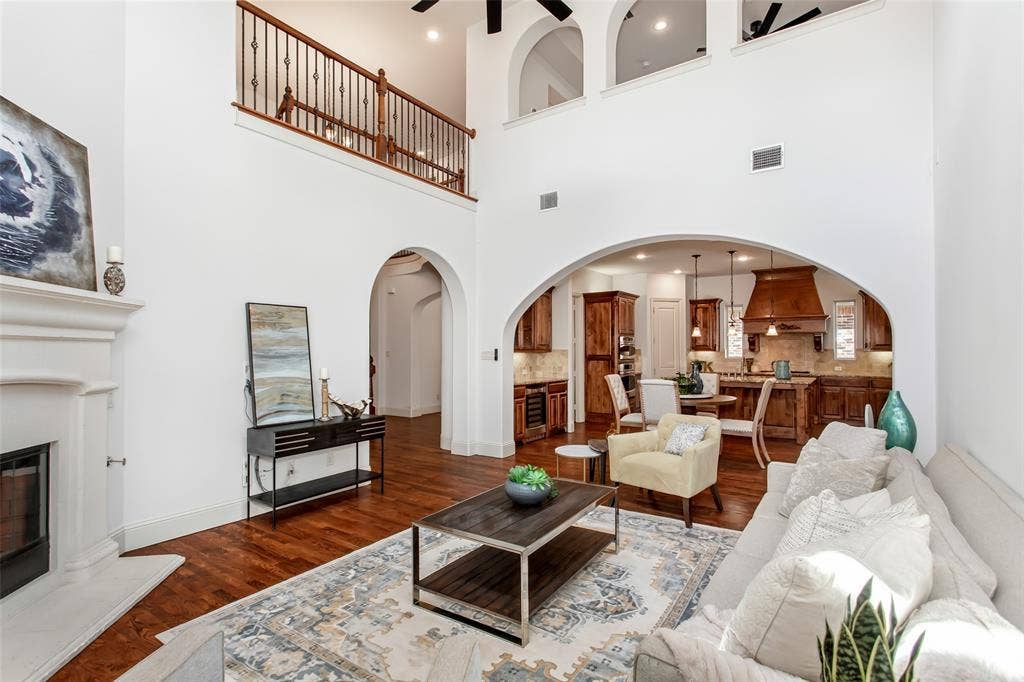 Two-story living area featuring a fireplace with a white mantel, an arched entry to the kitchen, and a second-story landing with an open railing