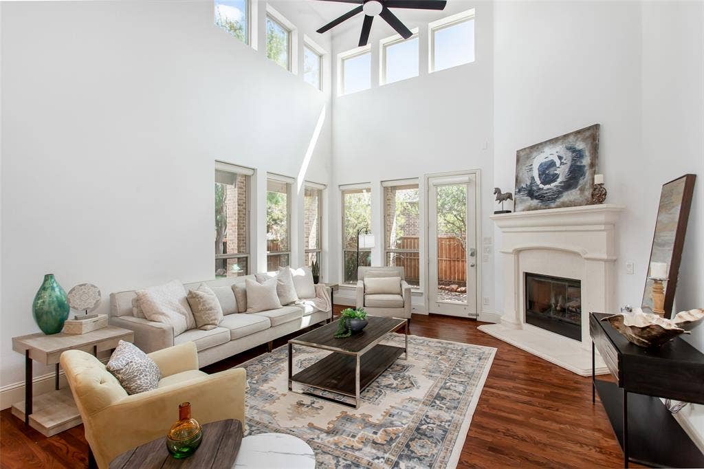 Expansive living area featuring a vaulted ceiling with a ceiling fan, a fireplace with a substantial mantel, multiple windows, and wood-finish flooring