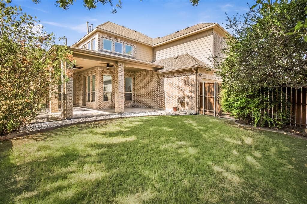 Expansive backyard featuring a covered patio, brick columns, and a manicured lawn
