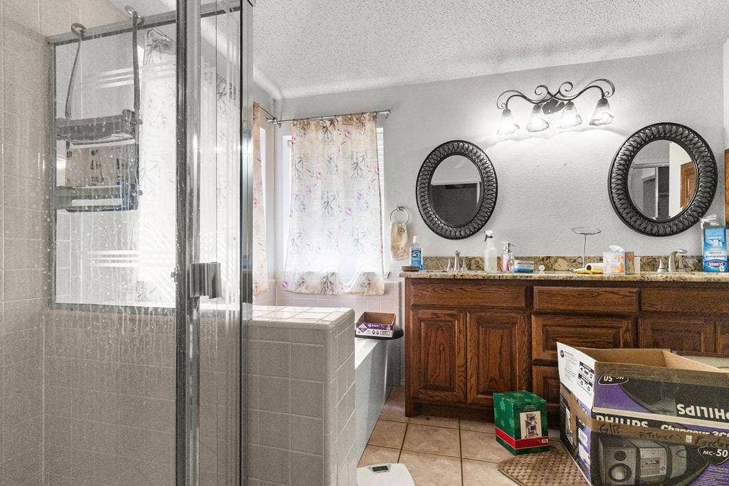 926 Wintercrest Court, Arlington, TX 76017 Enclosed shower with glass paneling, tile-surround bathtub, double vanity with wood cabinetry, dual oval mirrors, and a four-light vanity fixture
