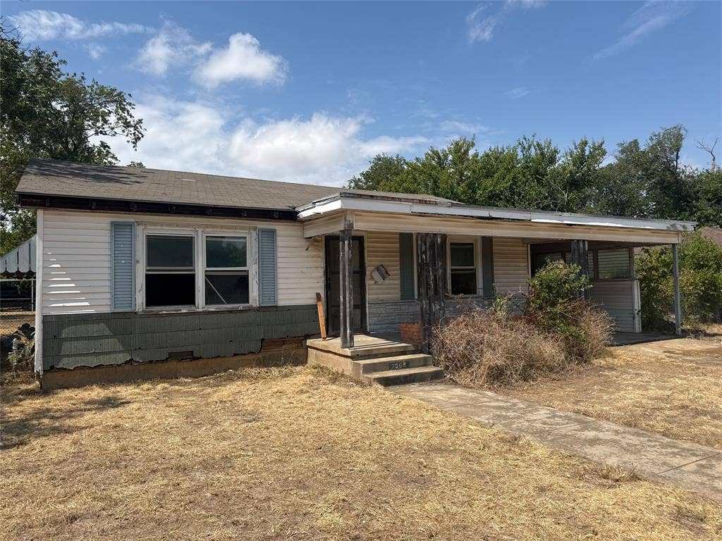 1305 W 11th Street, McGregor, TX 76657 Single-story residence featuring siding exterior, an extended covered porch, a concrete walkway, and mature trees in the background