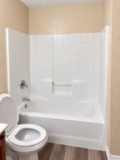 Bathtub with white surround and integrated grab bar, chrome fixtures, and wood-finish flooring