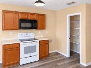 Wood-finish flooring, wood cabinetry, white countertops, built-in microwave, and a pantry with wire shelving