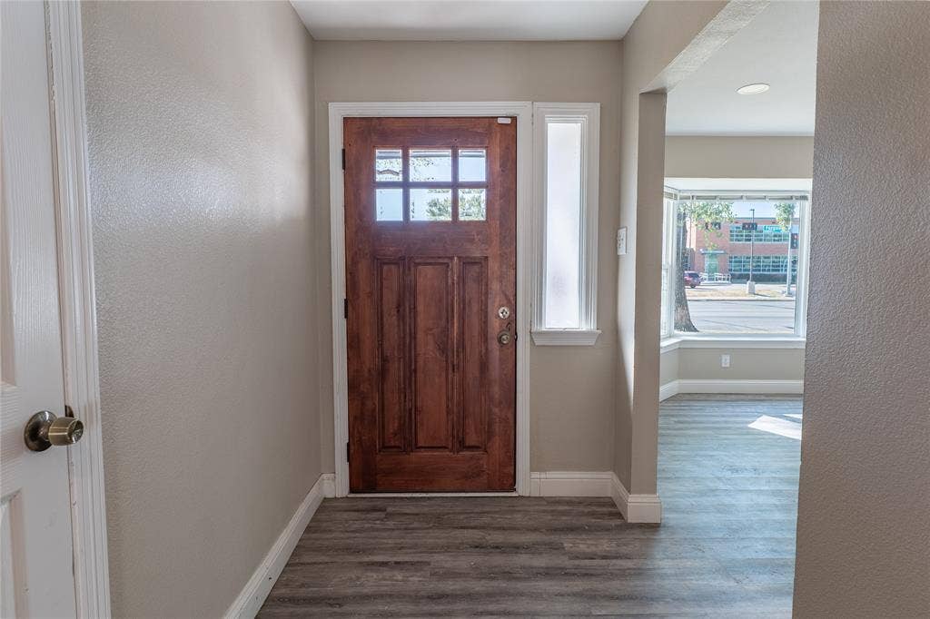 Wood-finish flooring, paneled entry door with glass inserts, transom window, and bay windows